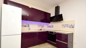Eine moderne Küche mit dunklen Schränken, einem weißen Kühlschrank, einem eingebauten Backofen und einem schwarzen Fernseher, der über der Arbeitsplatte angebracht ist.