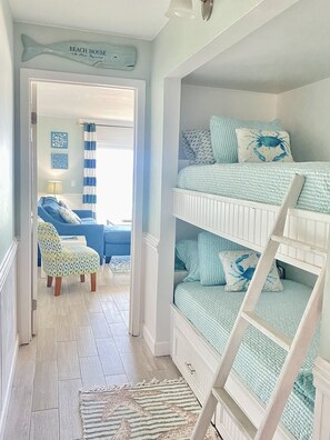 Habitación infantil con literas, una silla y una puerta que da a otra habitación.