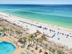 Ein Strandhotel mit Schwimmbad, Liegestühlen und Sandstrand.