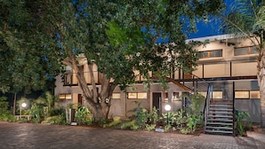 A modern building with a large tree in front, a staircase, and a paved driveway.