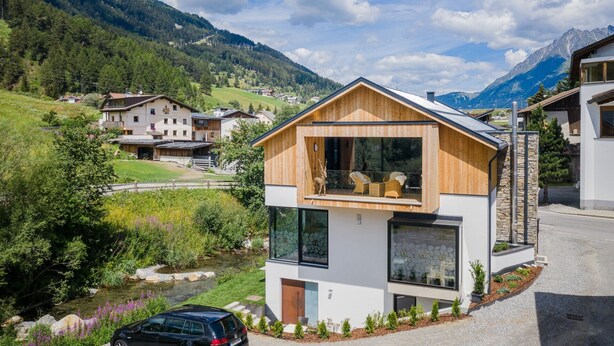 Une maison moderne avec une façade en bois, de grandes fenêtres et une vue sur une chaîne de montagnes.