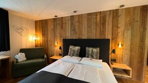 Une chambre d’hôtel avec un lambris en bois, un lit avec du linge de maison blanc, un fauteuil vert et deux lampes de chevet.