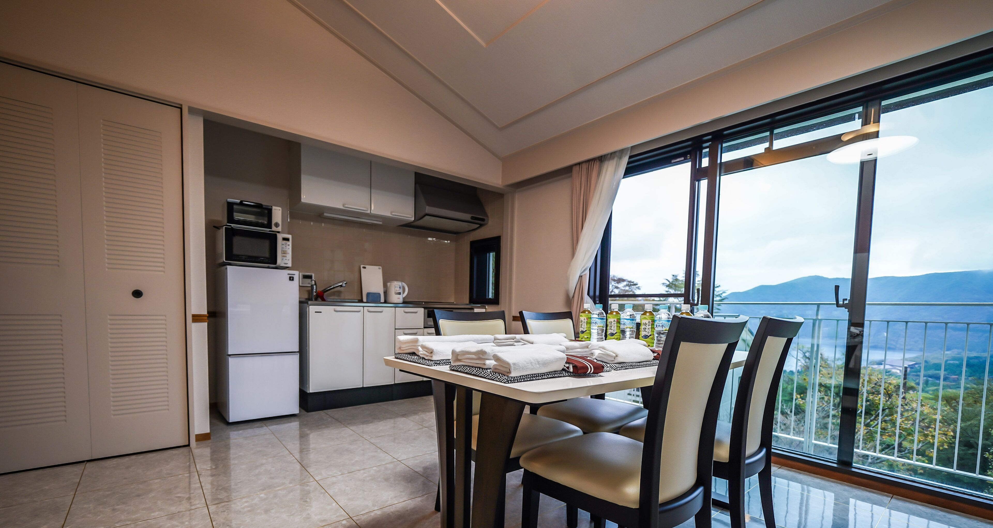 A modern kitchen with a dining area, large windows with a view, and a balcony.