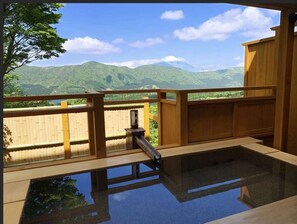 Una terraza de madera con piscina de fondo de cristal, que ofrece vistas a montañas verdes y un cielo despejado.