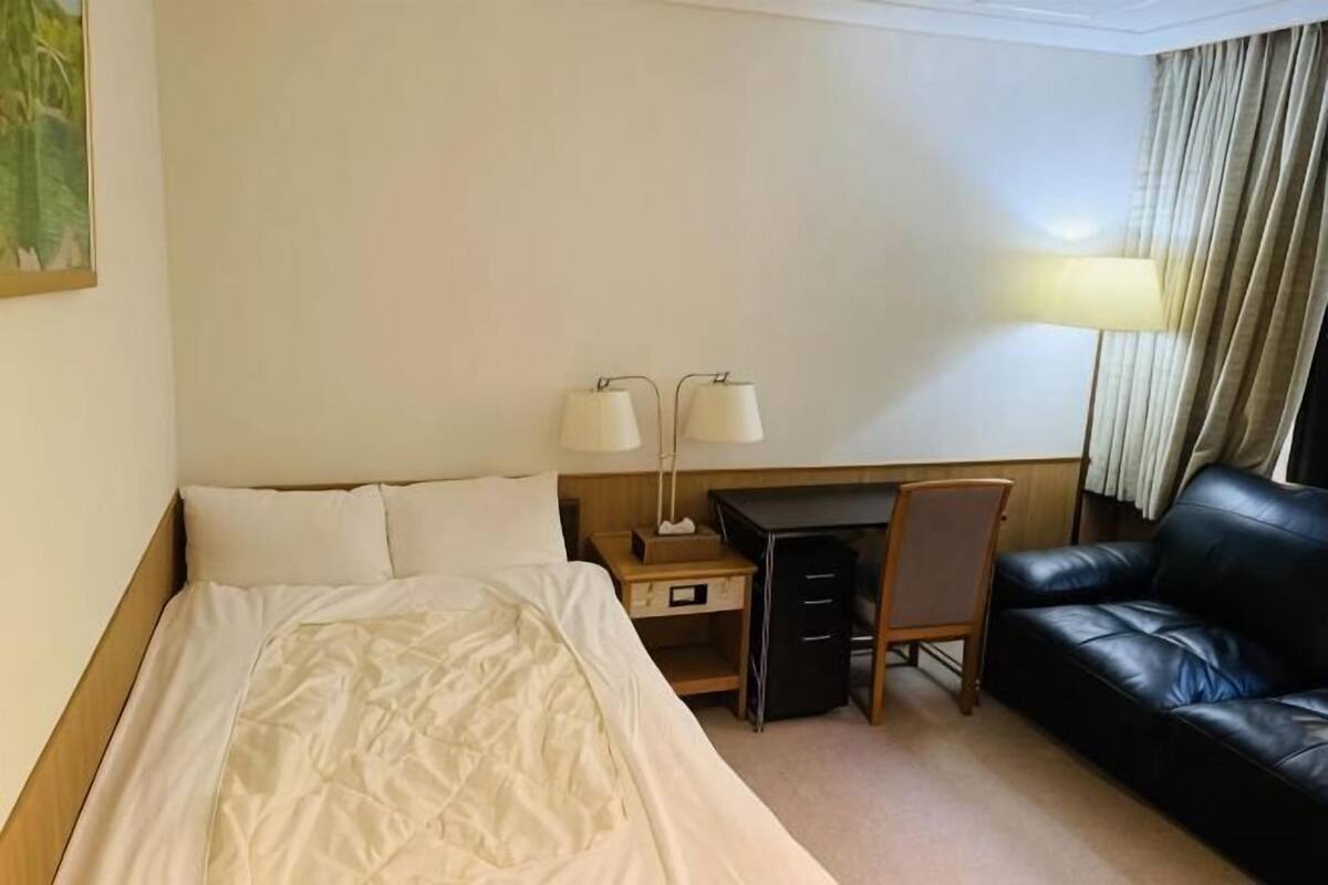 A hotel room with a bed, desk, chair, and a leather sofa.