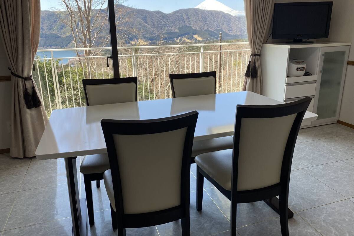 A dining area with a table and chairs, a television on a cabinet, and a view of a mountain and lake.