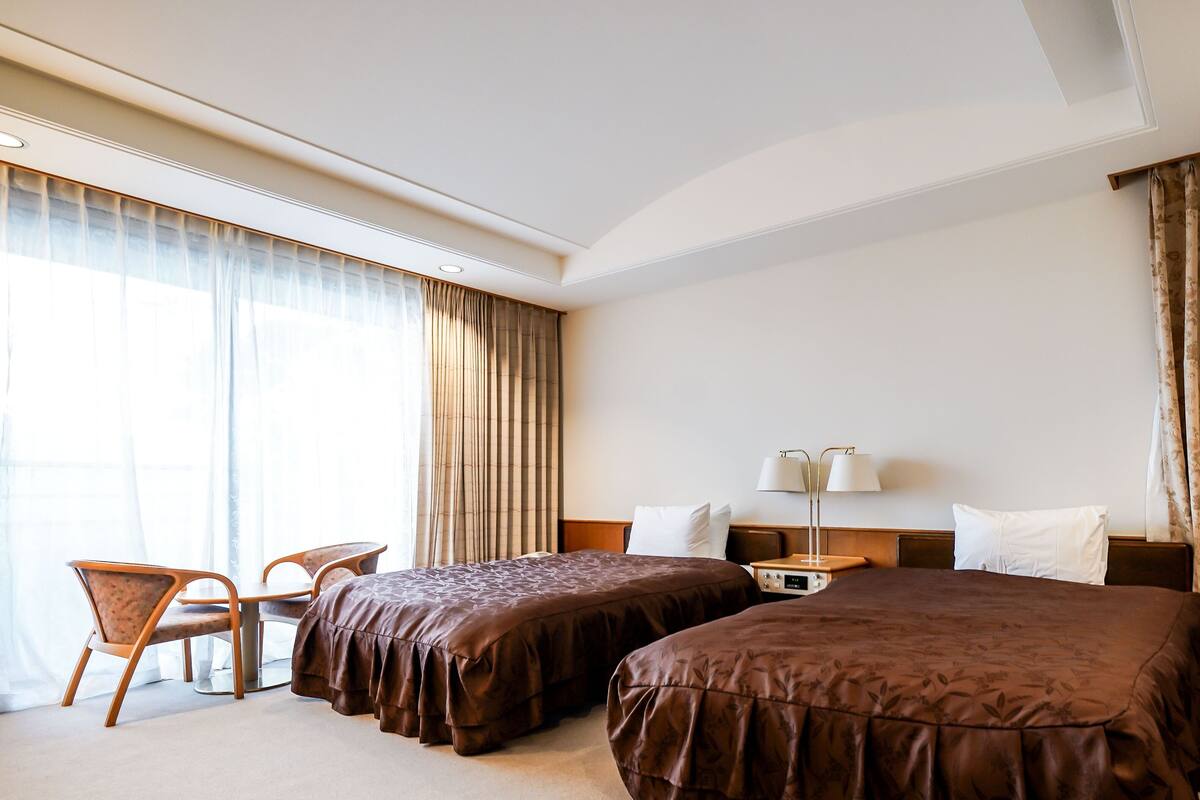 A hotel room with two beds, a desk, a chair, and a nightstand with lamps.