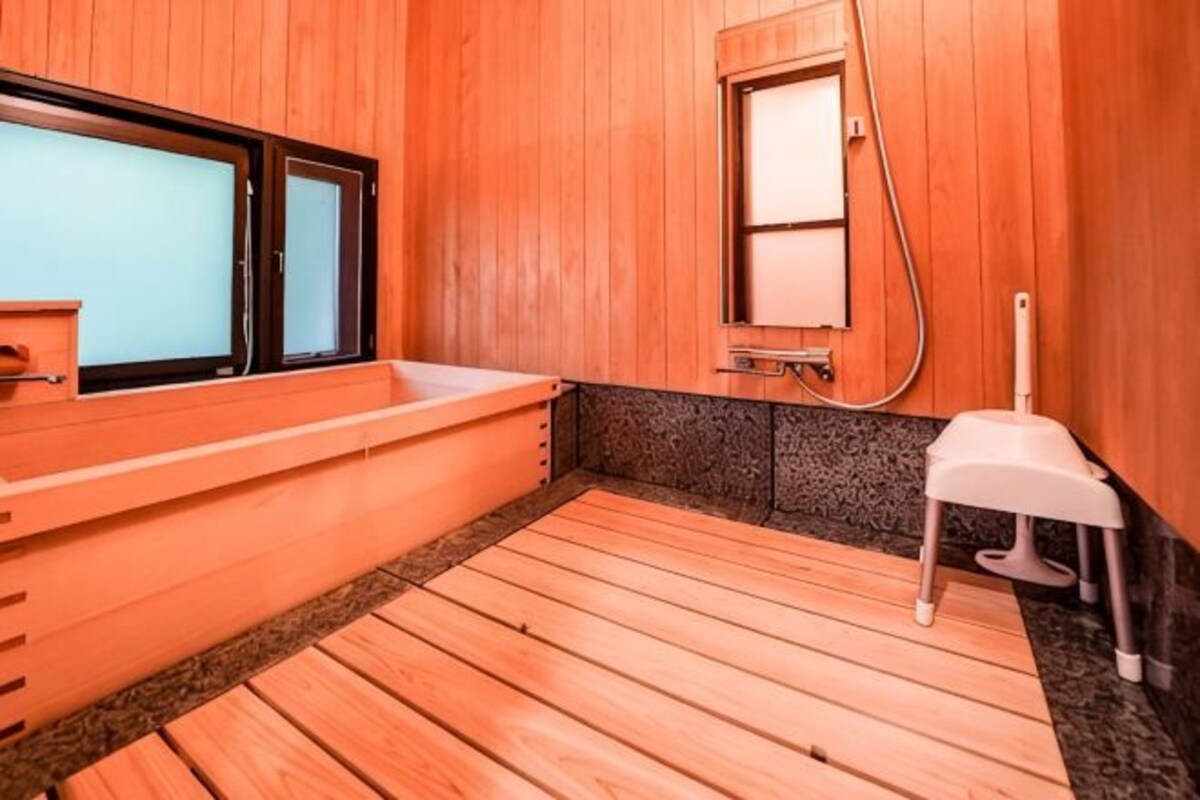 A sauna room with wooden flooring, a bench, a small table, and a window.