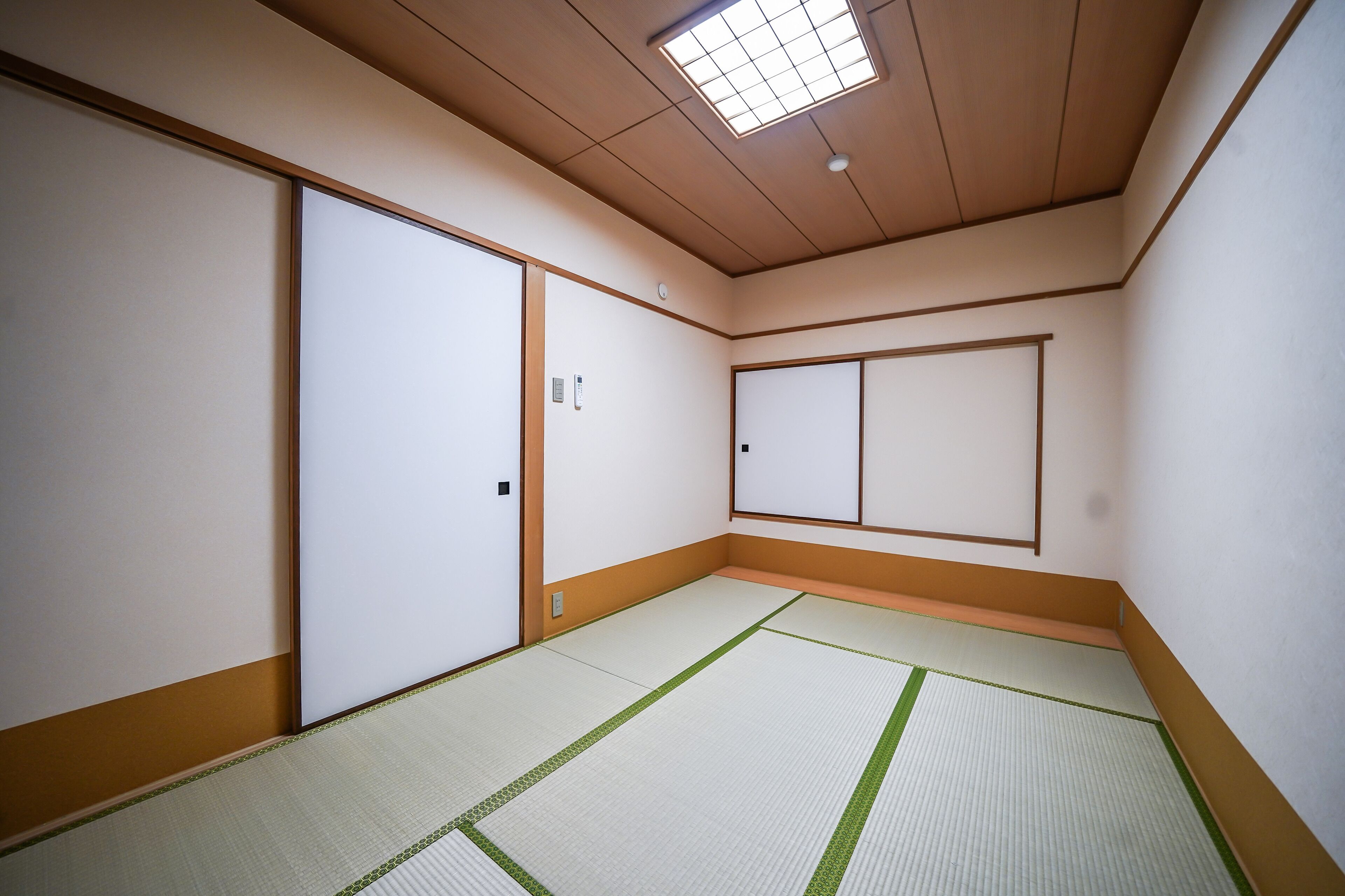 A traditional Japanese room with tatami flooring, sliding doors, and a ceiling light fixture.