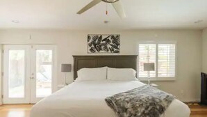 Une chambre à coucher avec un lit, un ventilateur de plafond, des œuvres d’art et des fenêtres.