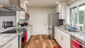 Une cuisine moderne dotée de plans de travail en granit, d’appareils électroménagers en acier inoxydable et d’un revêtement de sol en bois.