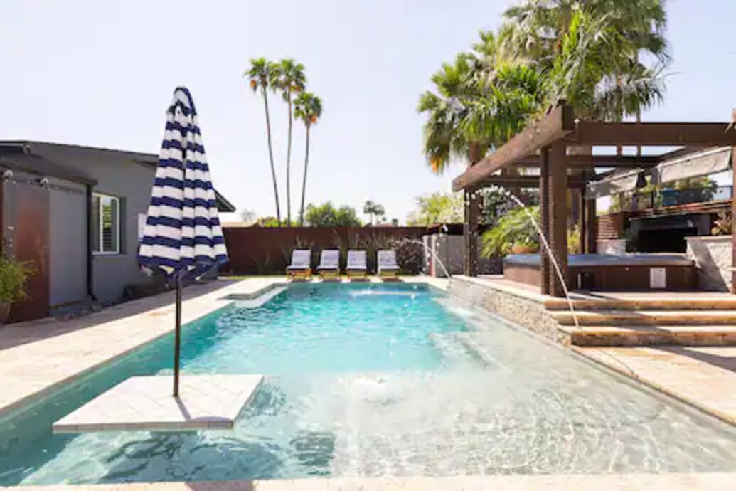 A swimming pool with lounge chairs and a striped umbrella.