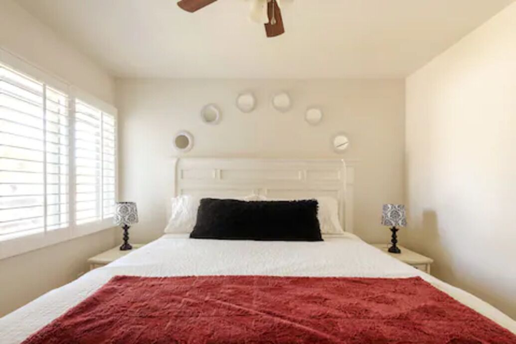 Ein Schlafzimmer mit einem weißen Bett, einer roten Tagesdecke, zwei Nachttischlampen und einem Deckenventilator.