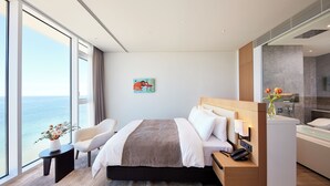 Habitación de hotel moderna con una cama grande, zona de estar, baño y vistas al océano.