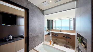 A modern kitchen with a built-in stove, a large window overlooking the sea, and a separate bathroom with a bathtub.