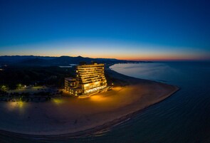 Un hotel frente a la playa con varios pisos, una playa de arena y vista al océano.