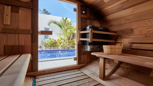 A wooden sauna with a bench, a wooden shelf with a bucket, and a Harvia sauna heater. - The Pool & Sauna Villa MOTOBU (Motobu)