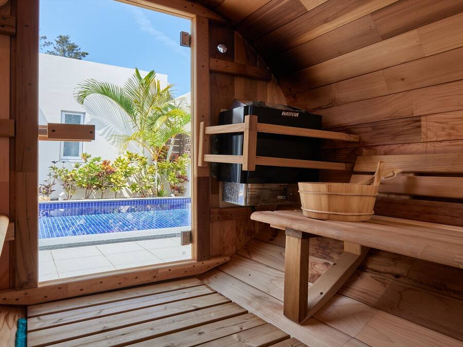 A wooden sauna with a bench, a wooden shelf with a bucket, and a Harvia sauna heater.