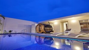 A modern indoor pool area with a clear blue pool, lounge chairs, and a wooden barrel. - The Pool & Sauna Villa MOTOBU (Motobu)