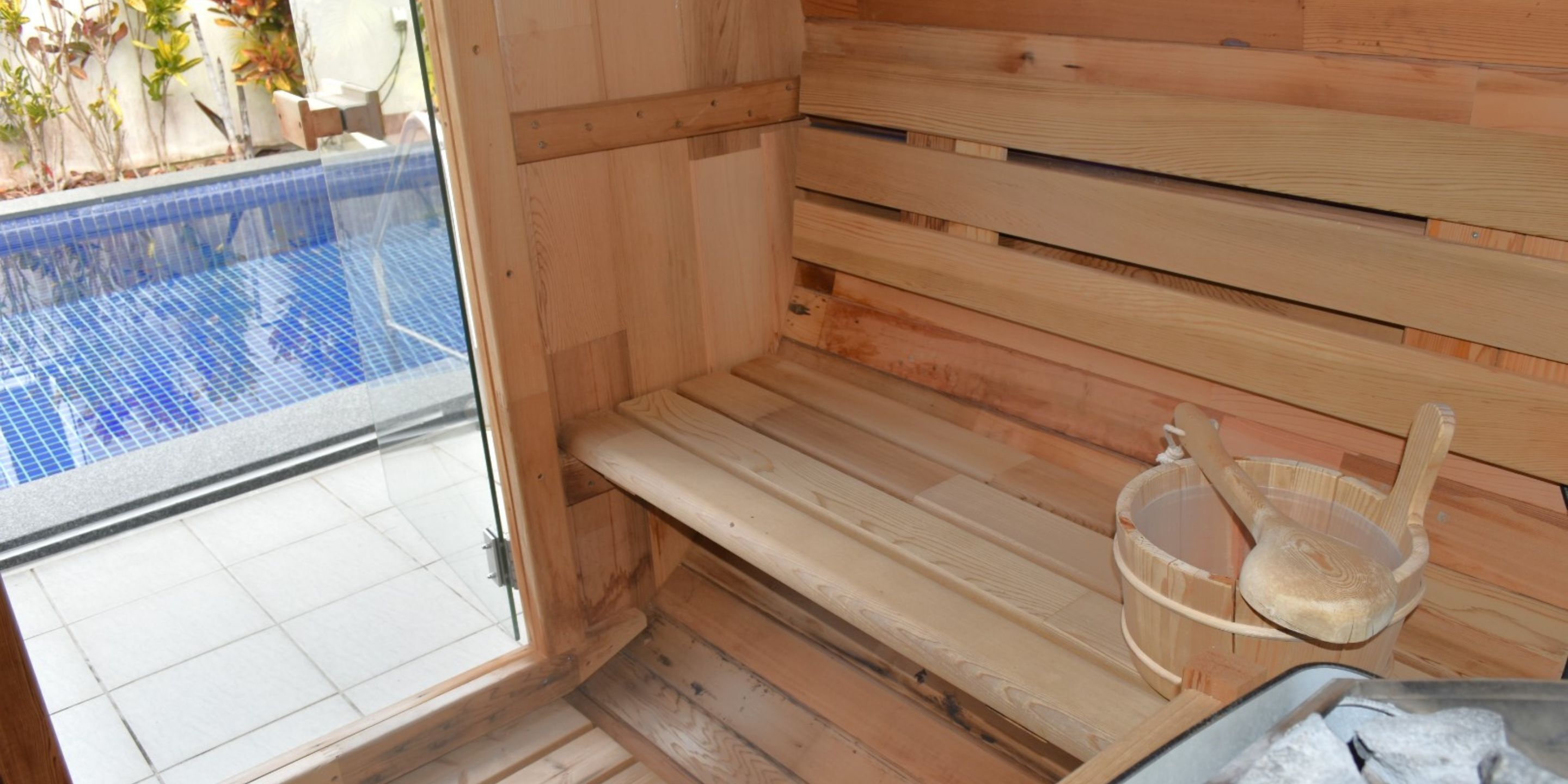 A sauna with wooden benches, a glass door, and a wooden bucket.