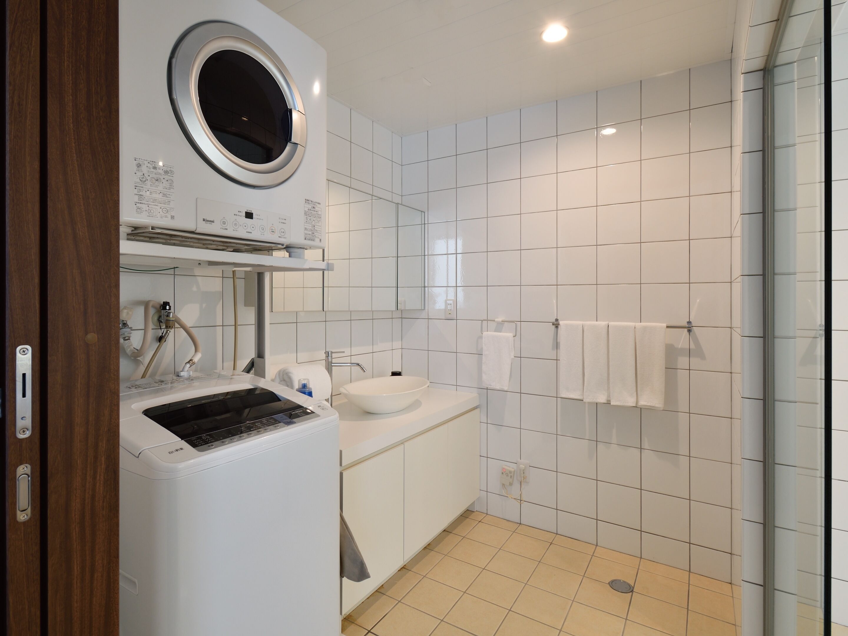 A modern bathroom with a built-in washer and dryer, a sink, and a glass shower enclosure.