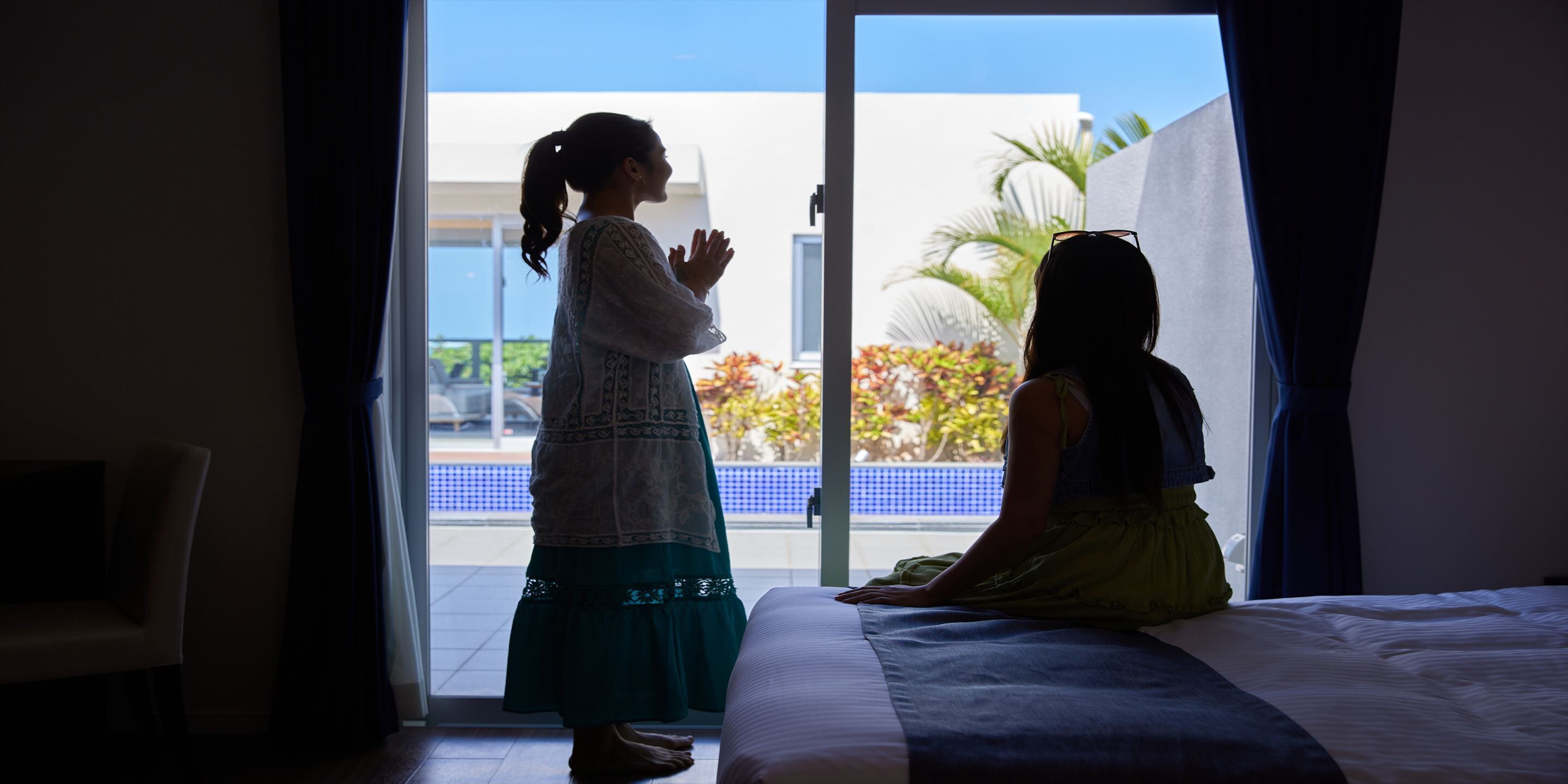 Ein Zimmer mit einem Bett, einem Sessel und Blick auf einen Pool und Palmen durch eine Glasdoor.