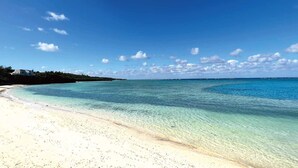 A beach with clear turquoise water, a sandy shore, and a few buildings in the background. - The Pool & Sauna Villa MOTOBU (Motobu)