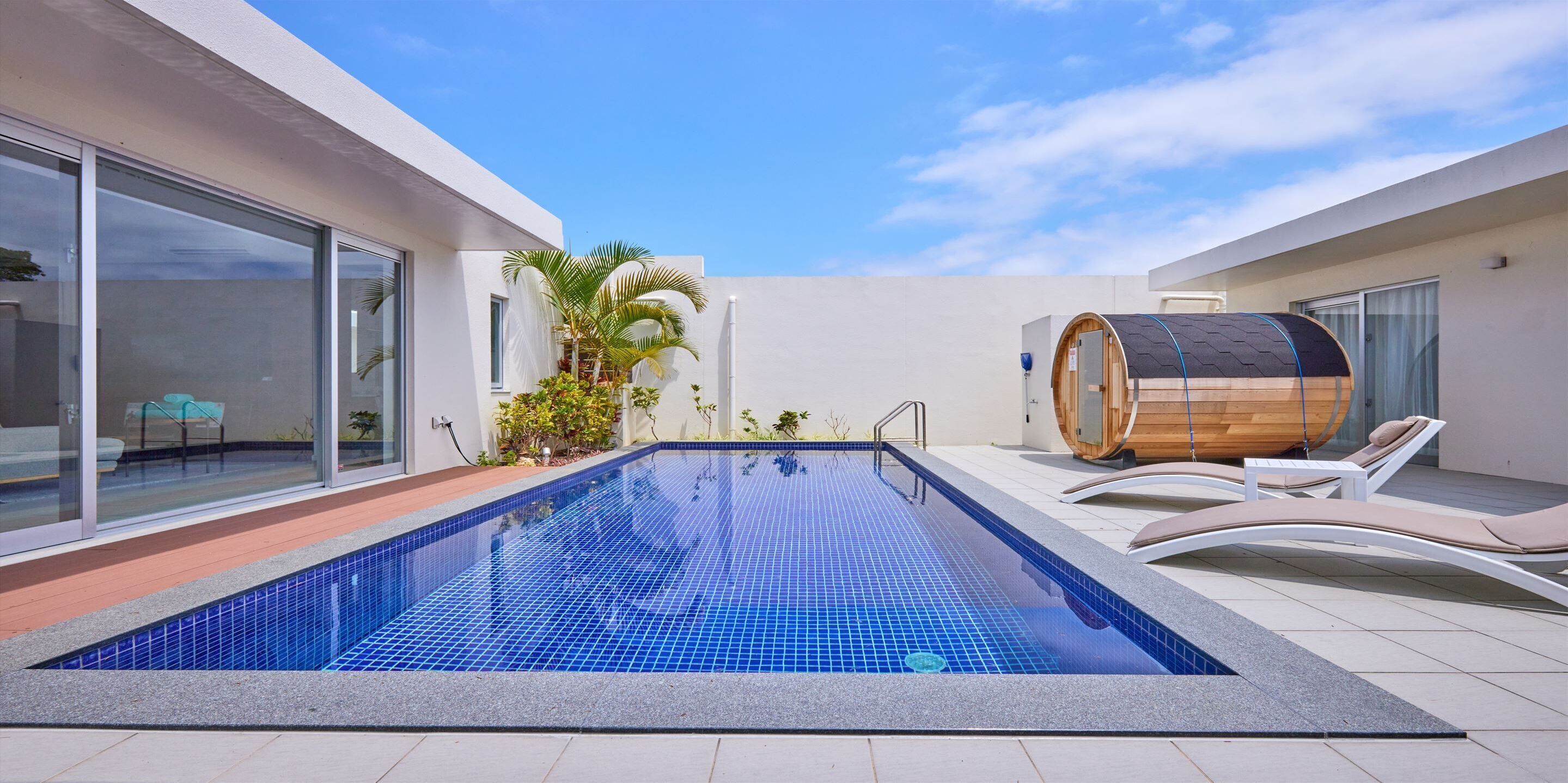 A modern outdoor swimming pool with lounge chairs and a sauna.
