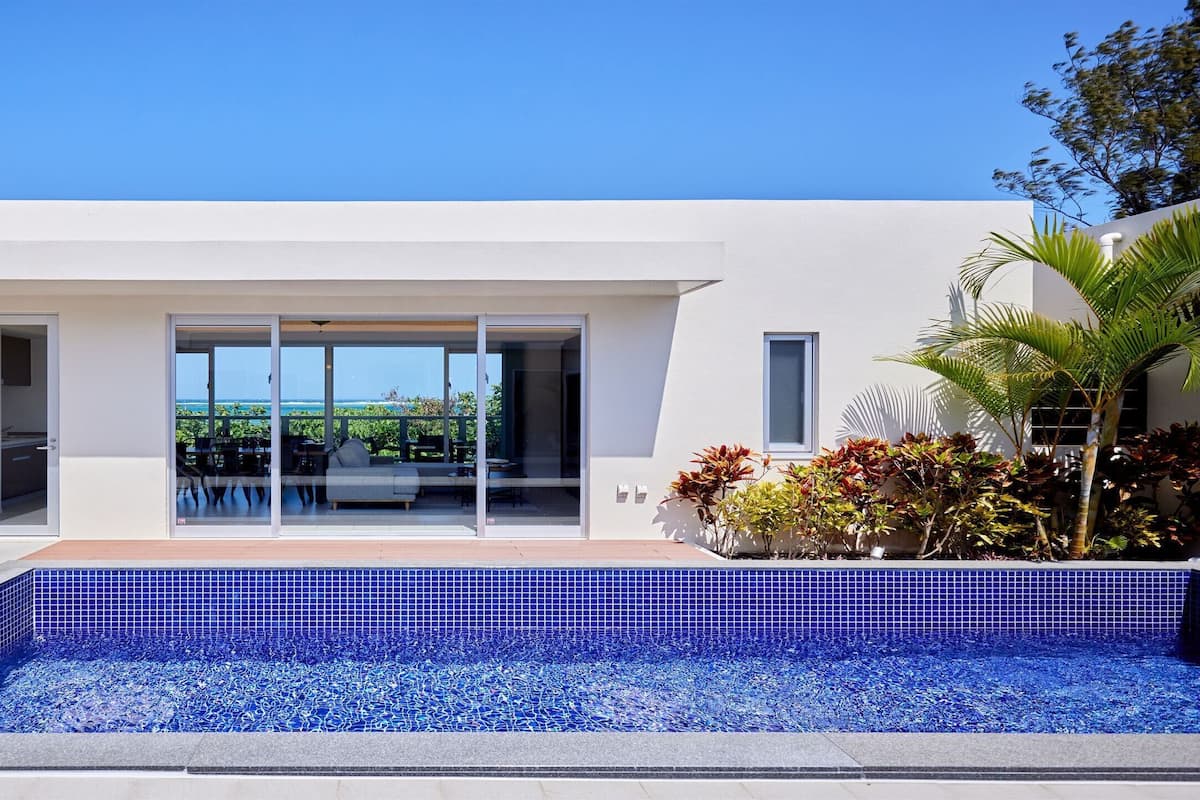 Ett modernt hus med en swimmingpool, stora glasdörrar och utsikt över havet.