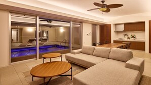 A modern living room with a sofa, two wooden side tables, a ceiling fan, and a glass-enclosed hot tub area. - The Pool & Sauna Villa MOTOBU (Motobu)