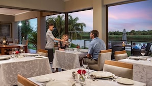 Un restaurante con mesas dispuestas para comer, un camarero atendiendo a los comensales y vistas a un cuerpo de agua y vegetación.