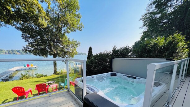 A hot tub on a deck with a view of a lake and chairs.