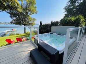A hot tub on a deck with a view of a lake and chairs.
