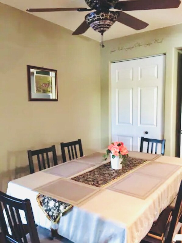 A dining area with a table set for six, a ceiling fan, and a door in the background.