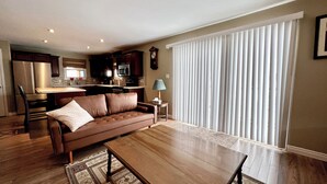 A living room with a brown sofa, a wooden coffee table, and a dining area with a kitchen in the background.