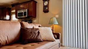A living room with a brown leather sofa, a wooden cabinet, a microwave, and a clock on the wall.