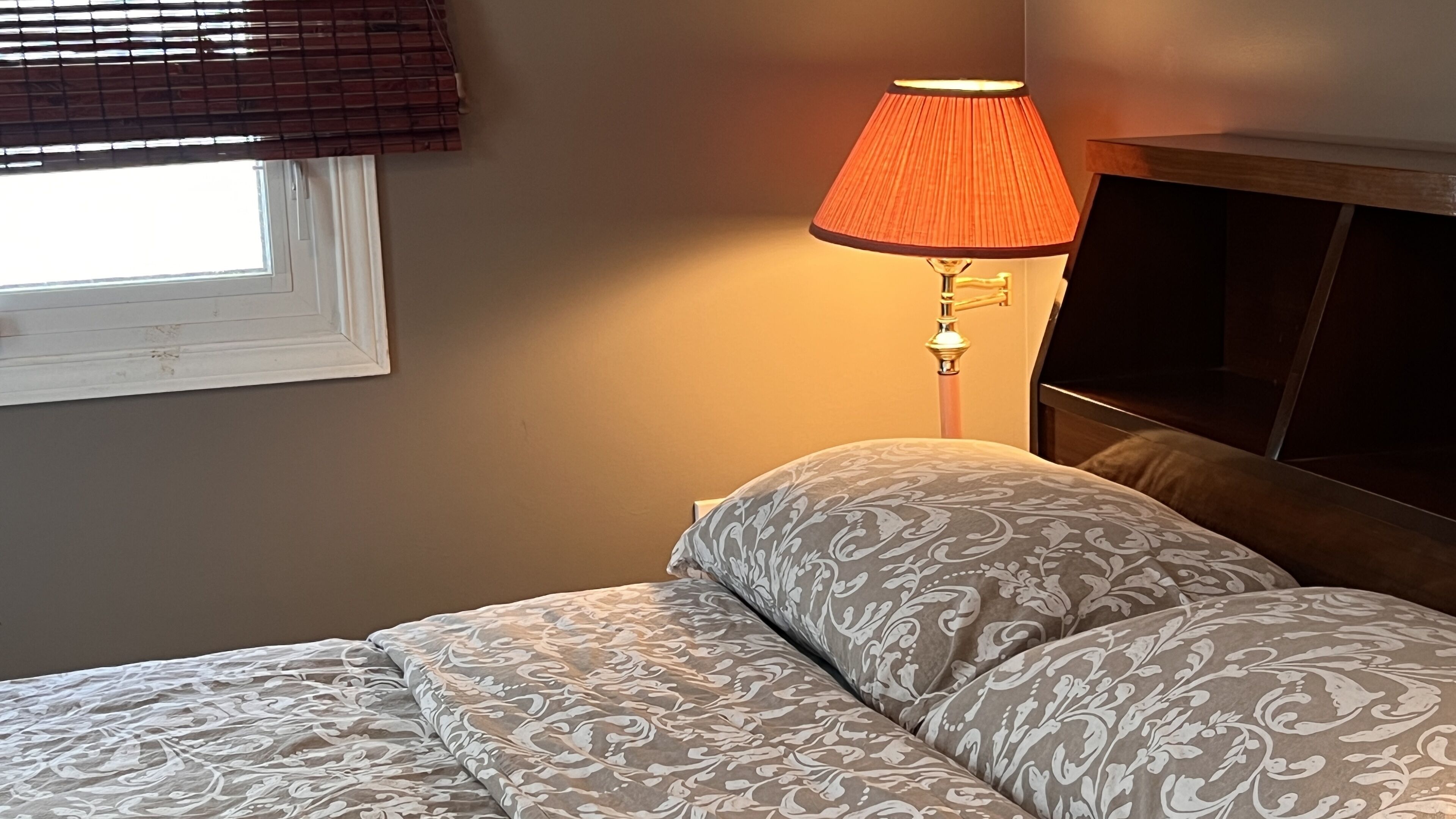 A bedroom with a bed, a window with blinds, and a bedside lamp.