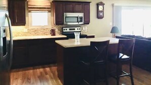 A kitchen with dark wooden cabinets, a microwave, a stove, and a coffee maker. There is a window with blinds and a clock on the wall.