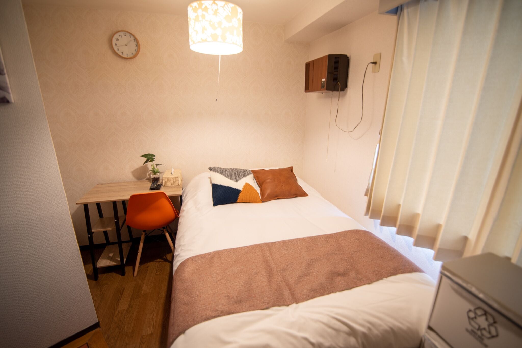 Un dormitorio con cama, escritorio, silla, reloj y ventana con cortinas.