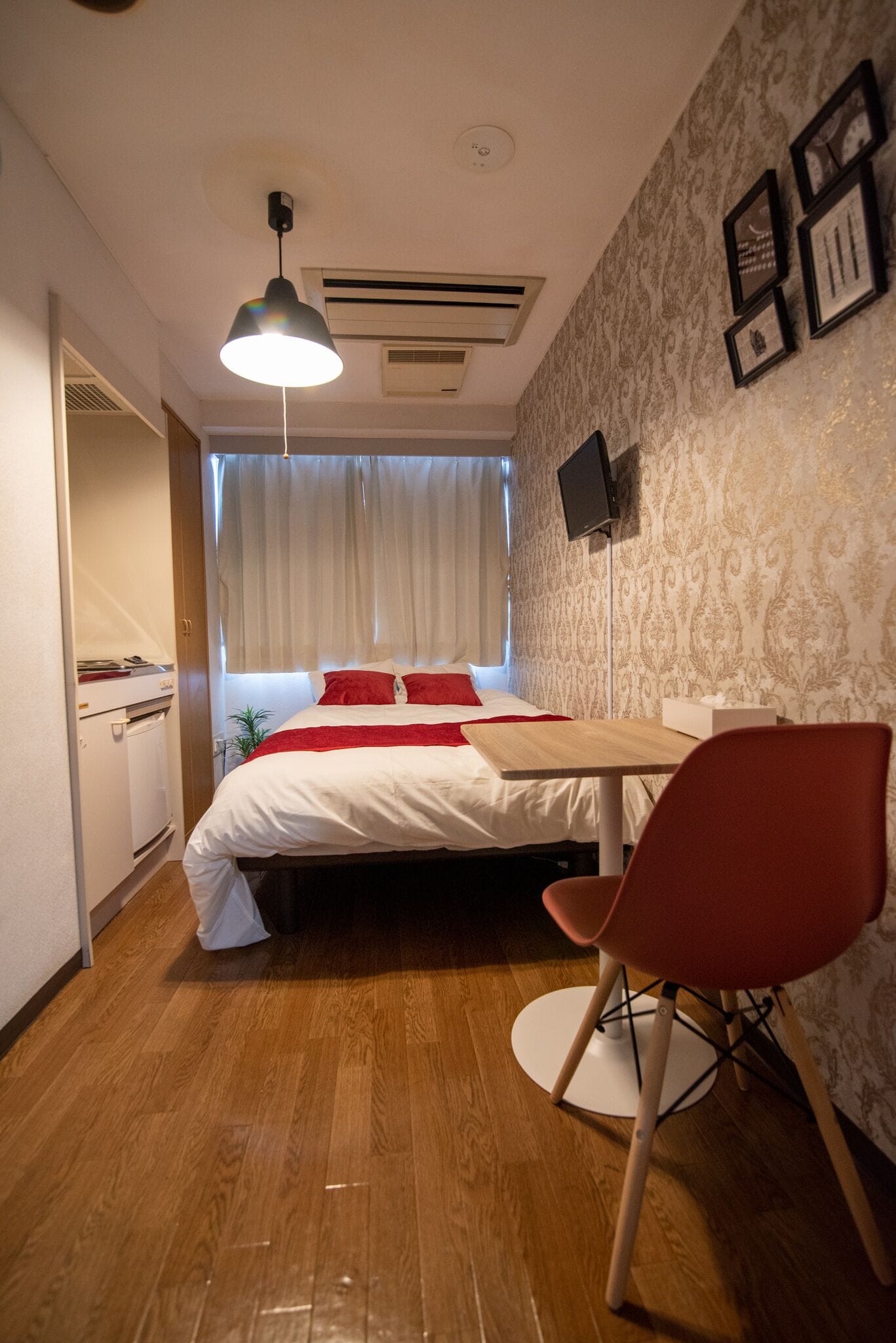 A bedroom with a bed, a desk, a chair, a television, and a window with curtains.
