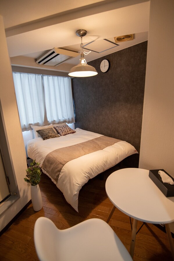 A compact hotel room with a bed, bedside table, and a small seating area.
