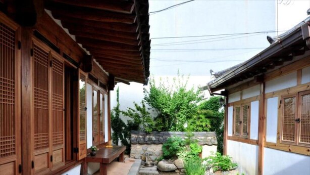 Un patio japonés tradicional con edificios de madera, un camino de piedra y vegetación.