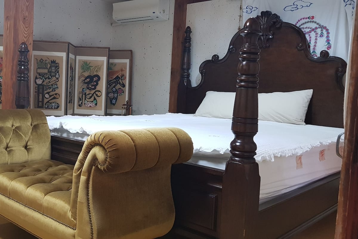 A bedroom with a four-poster bed, a tufted armchair, and a wooden cabinet with glass doors.