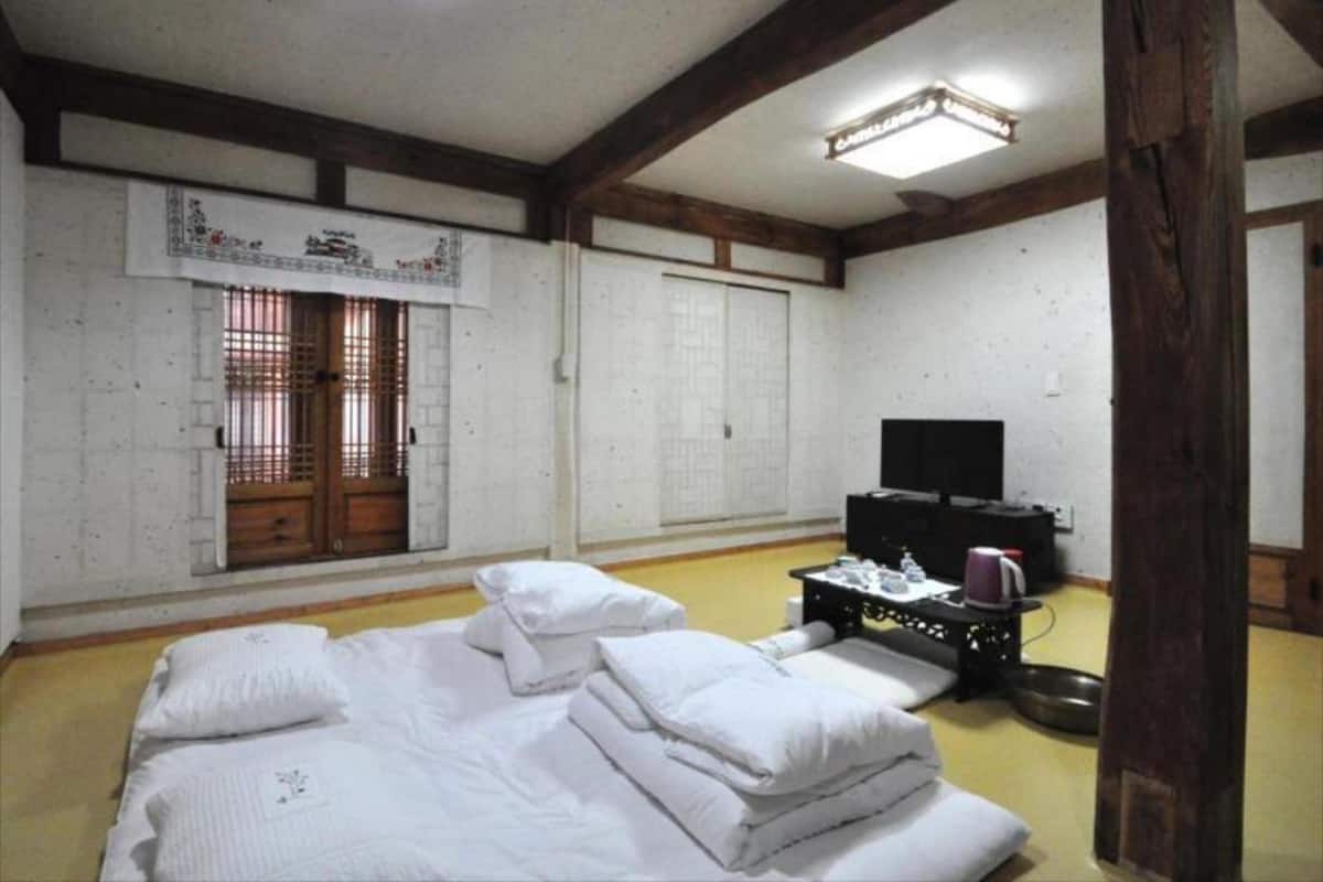 A traditional Japanese-style room with tatami flooring, a futon bed, a television, and a sliding door.