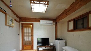 Habitación con techo de madera, un televisor sobre un mueble bajo, un refrigerador pequeño y una cama tipo futón.