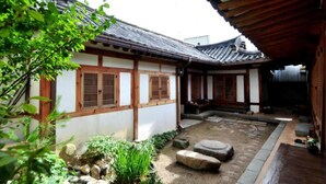 Un patio japonés tradicional con edificios de madera, un farol de piedra y un pequeño jardín.
