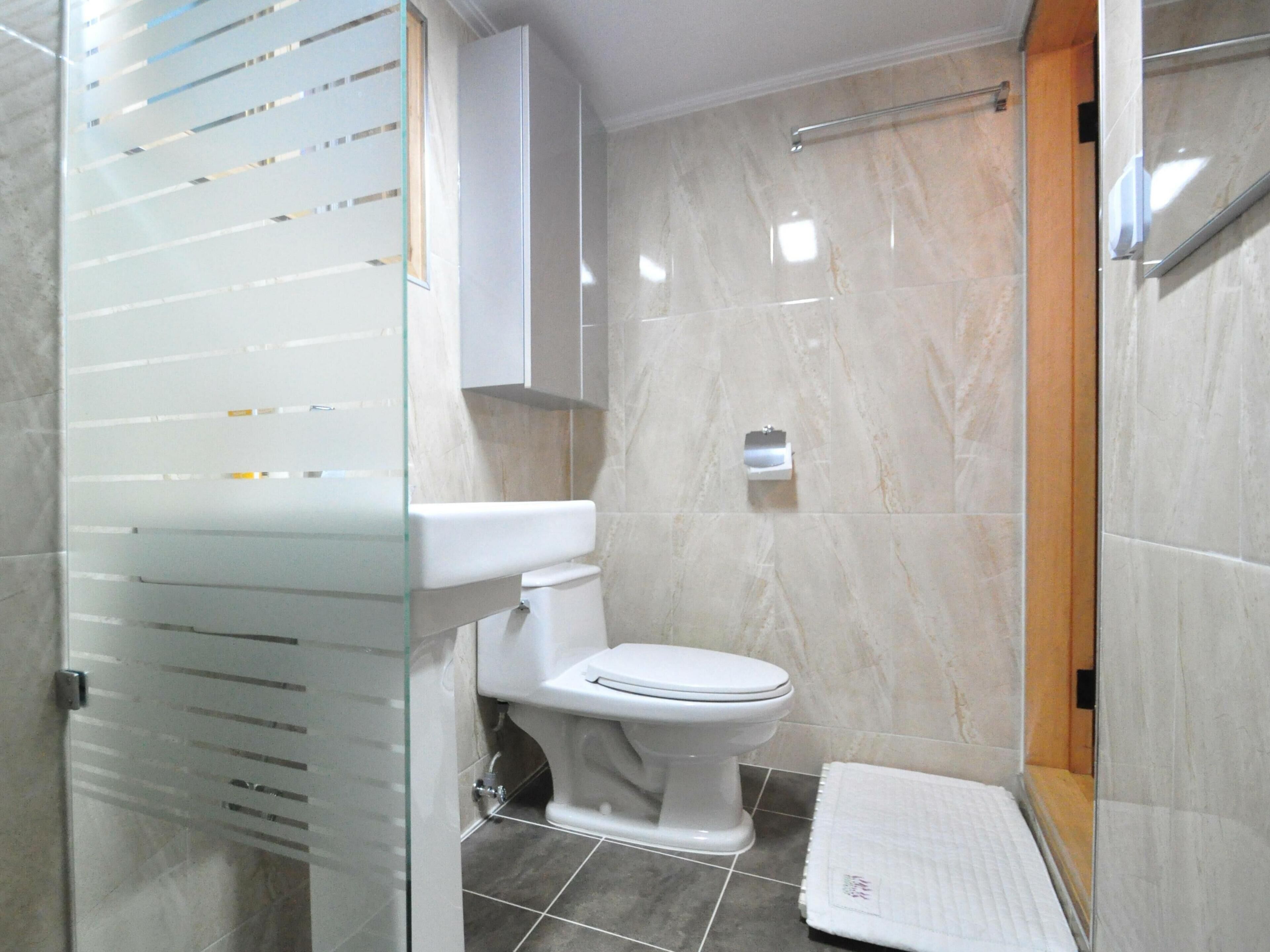 A modern bathroom with a toilet, a glass shower enclosure, and a tiled floor.