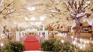 Un espacio para eventos formales con alfombra roja, decoración floral blanca y mesas dispuestas a ambos lados.