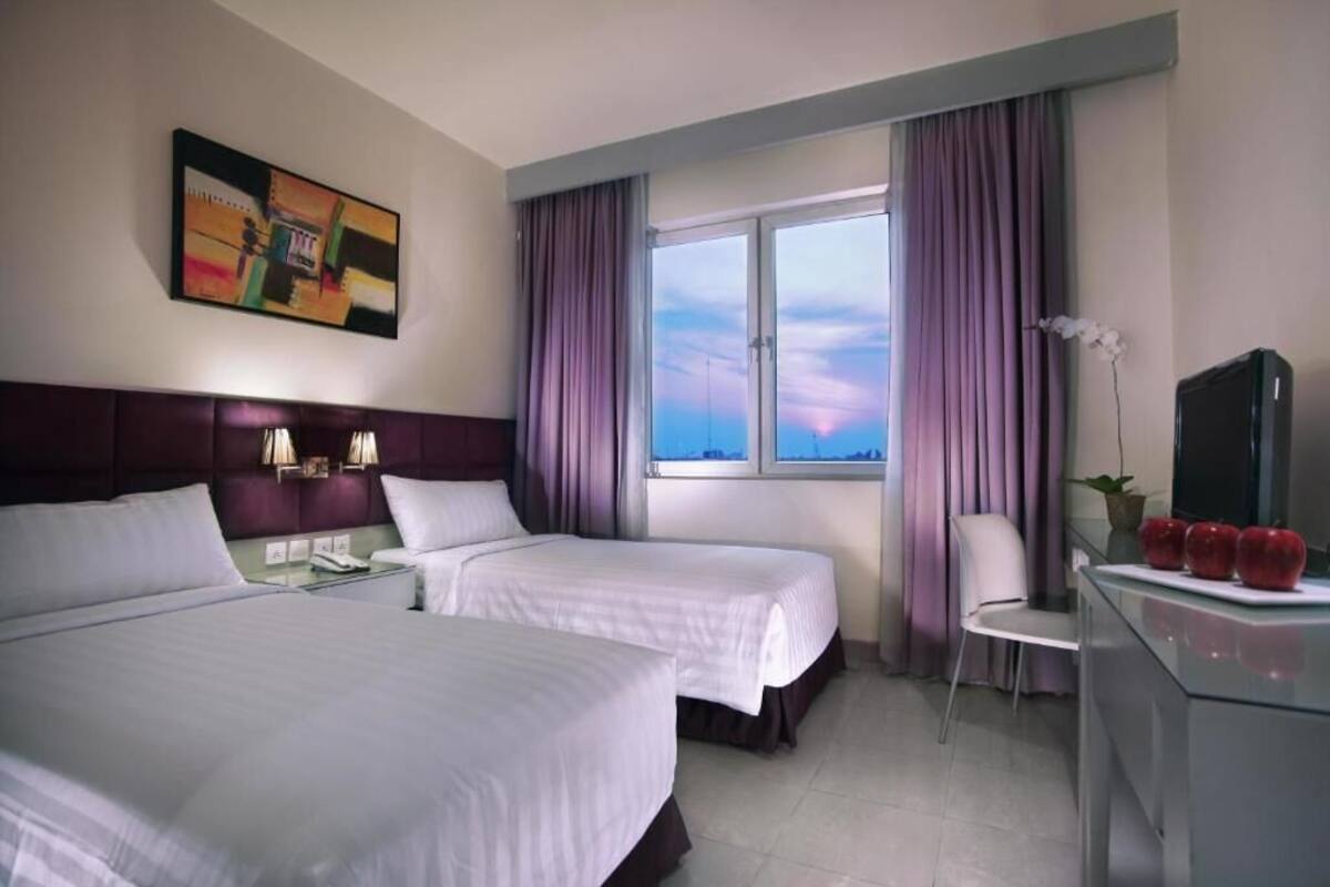 A hotel room with two beds, a desk with a TV, a chair, and a window with curtains.