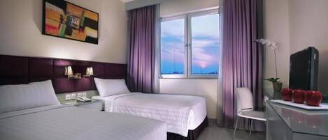 Habitación de hotel con dos camas, un escritorio con televisor, una silla y una ventana con cortinas.